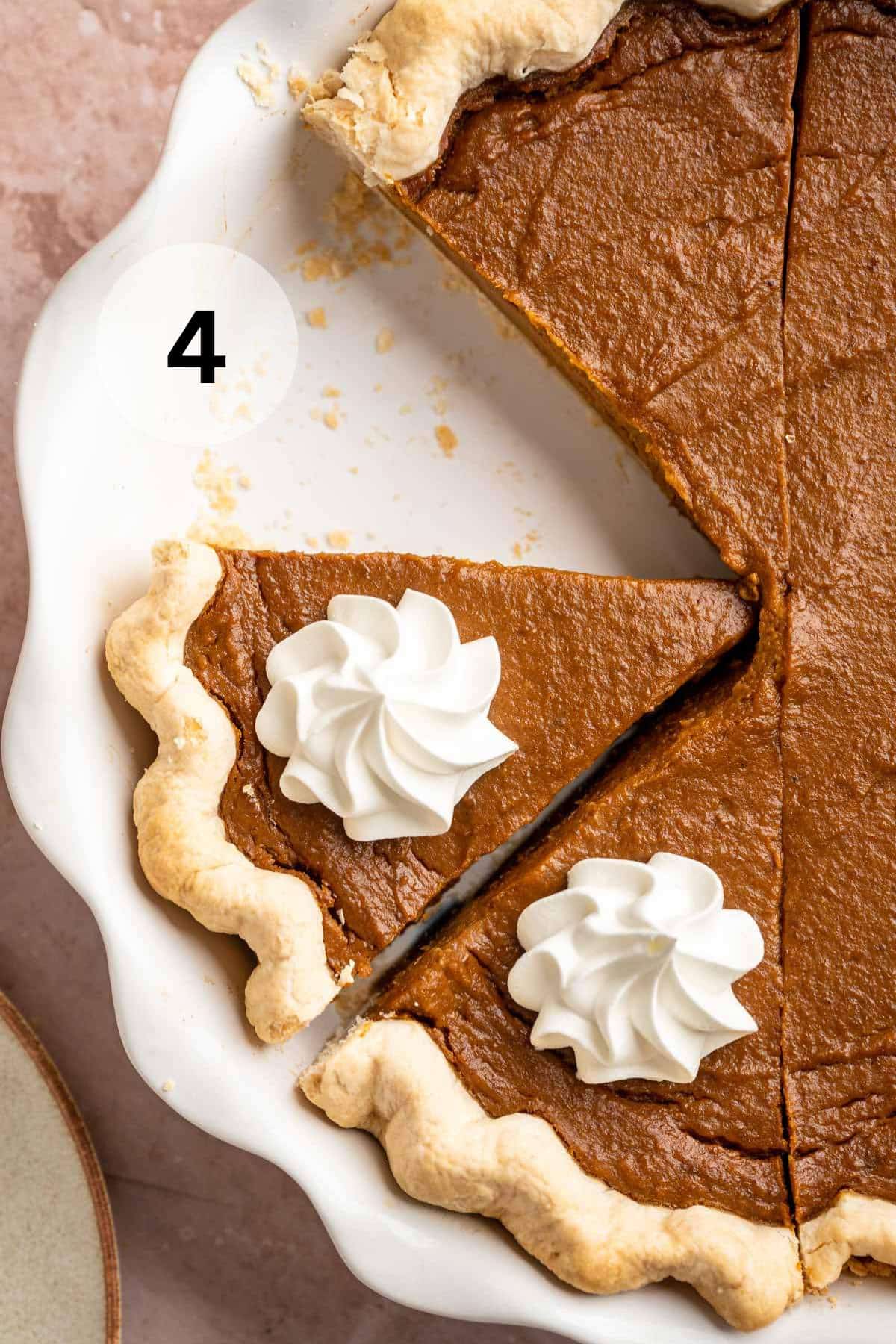 Pumpkin pie sliced in a pie plate and topped with whipped cream.