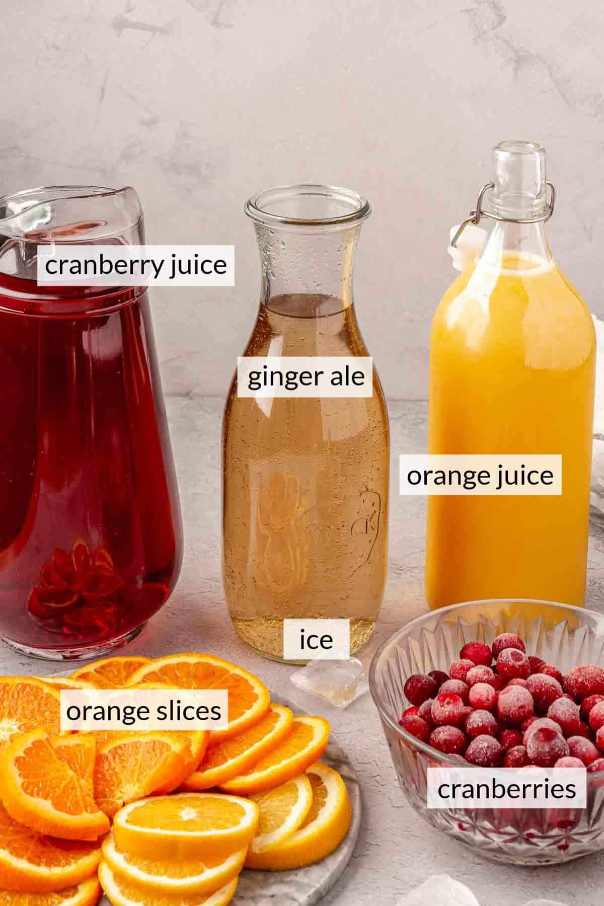 Glass bottles with cranberry juice, ginger ale and orange juice near freshly sliced oranges and frozen cranberries.