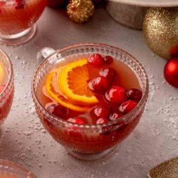 Christmas punch served in a small glass with orange slices and cranberries.