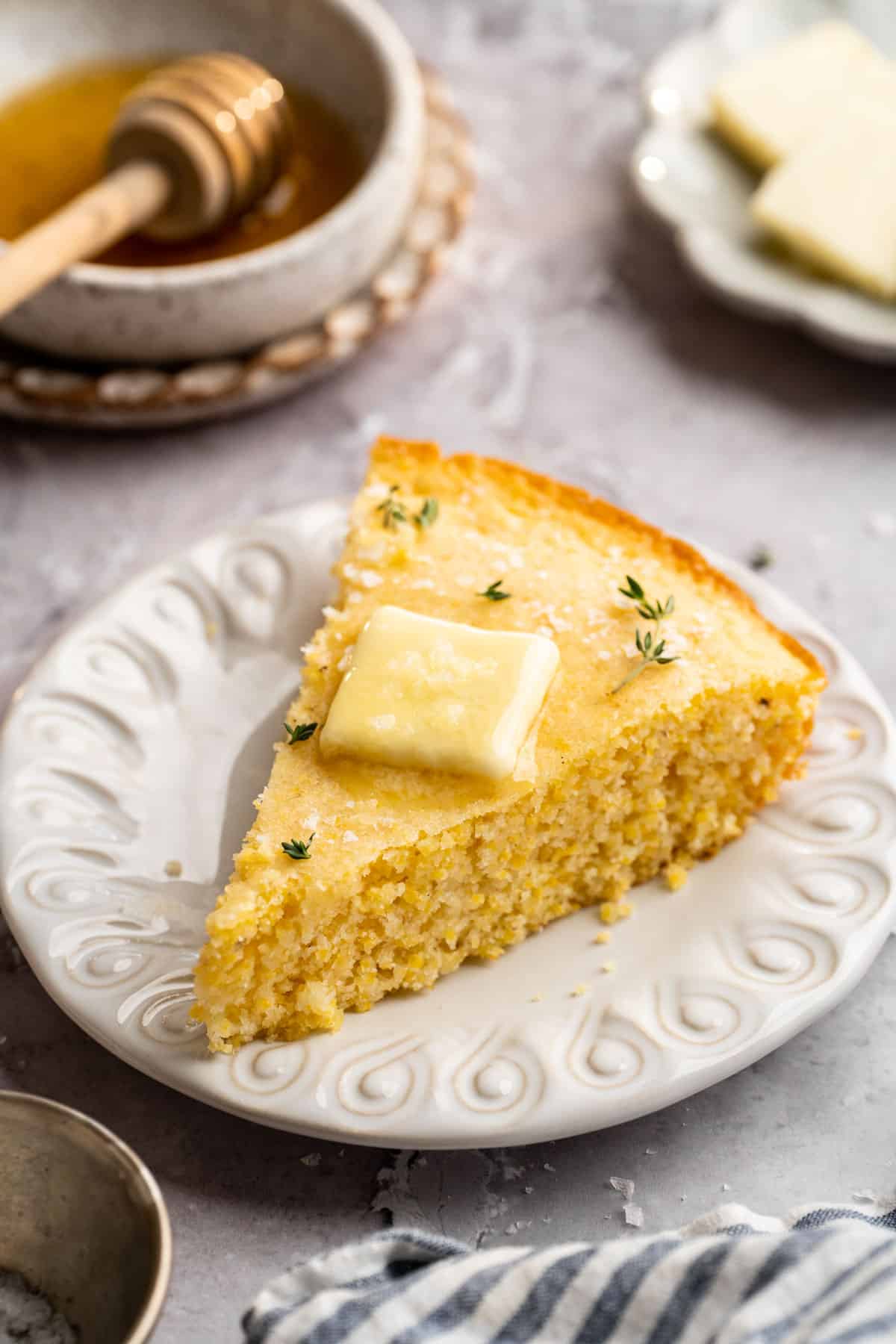 Slice of cornbread with butter on a white plate.