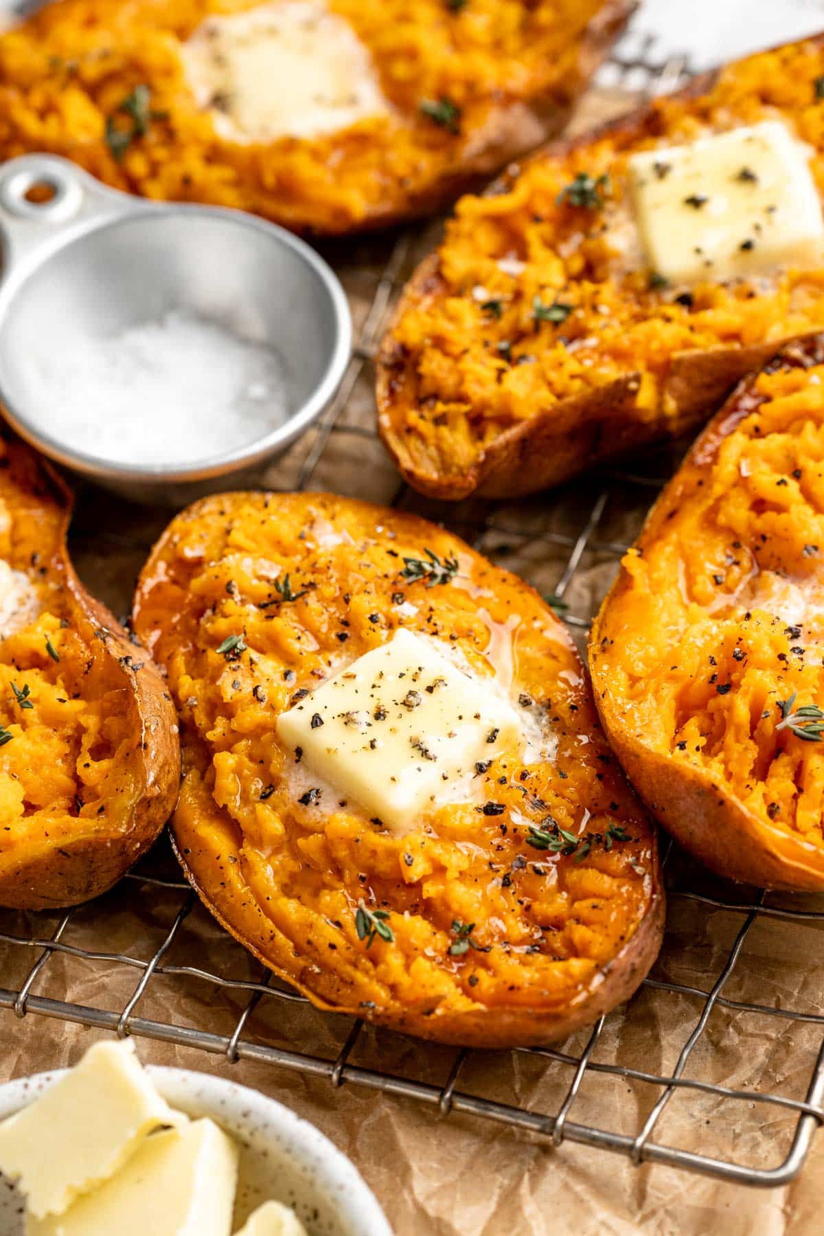 Baked sweet potatoes on a wire rack topped with a pat of butter and herbs.
