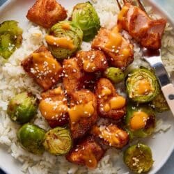 Air fryer salmon bites on a plate with rice and Brussels sprouts and topped with sesame seeds.