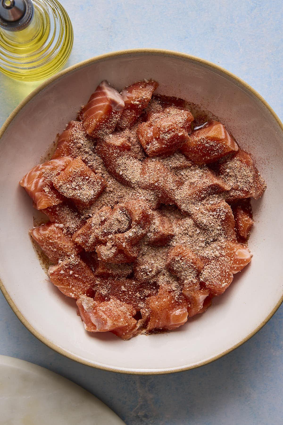 Chunks of salmon in a bowl with spices on top.