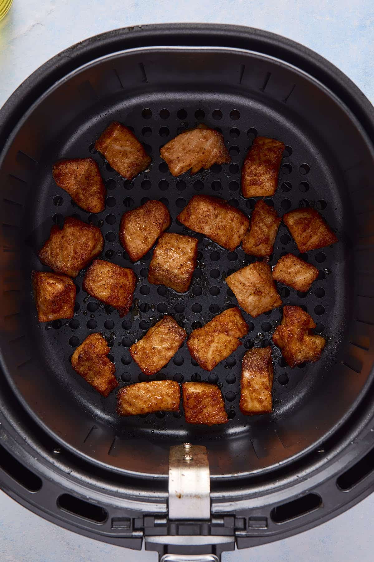 Cooked chunks of salmon in an air fryer basket.