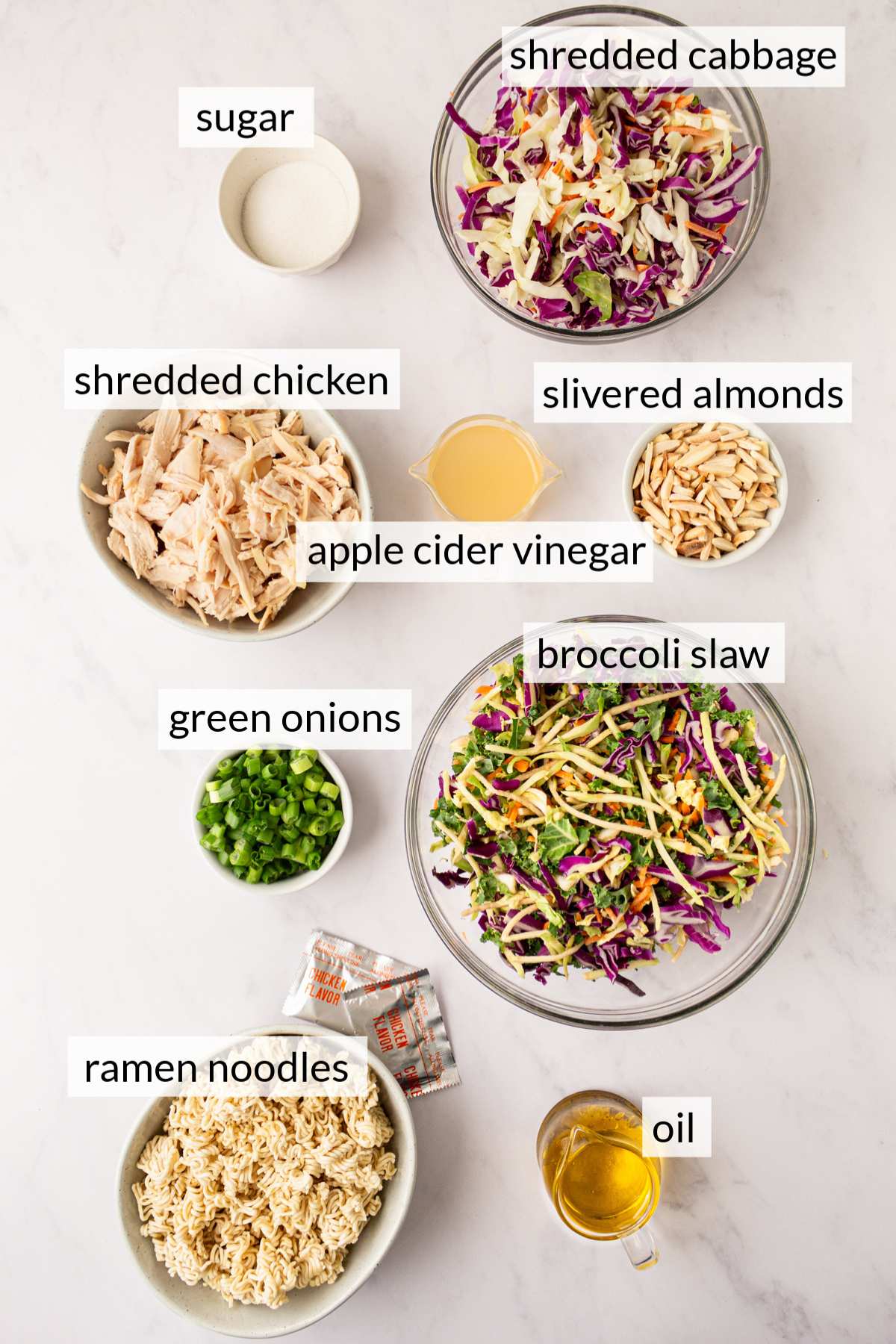 Small bowls with ingredients like shredded cabbage, broccoli slaw, ramen noodles, green onions, shredded chicken and oil.