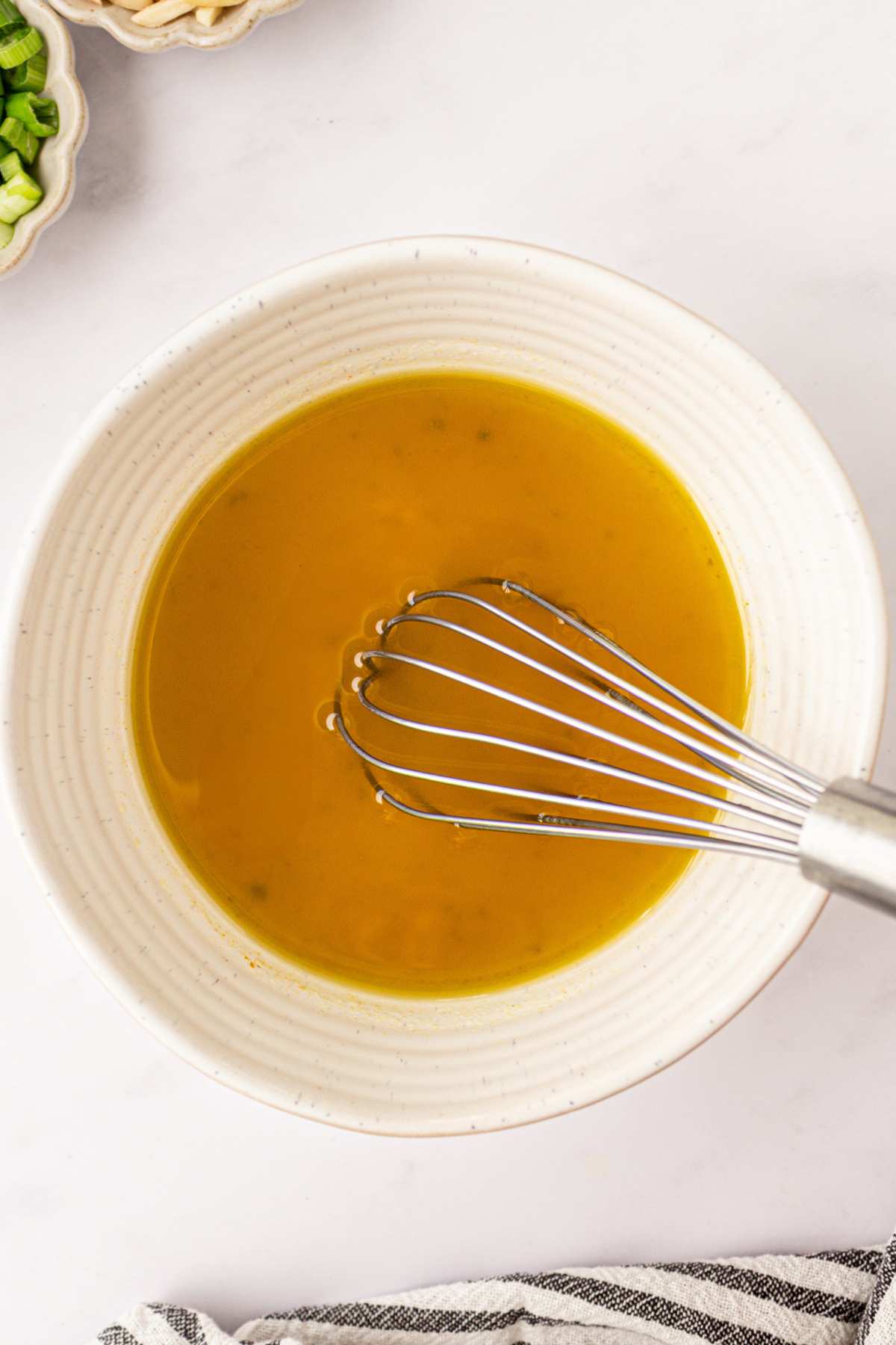 Whisking oil with apple cider vinegar and sugar in a small white bowl.