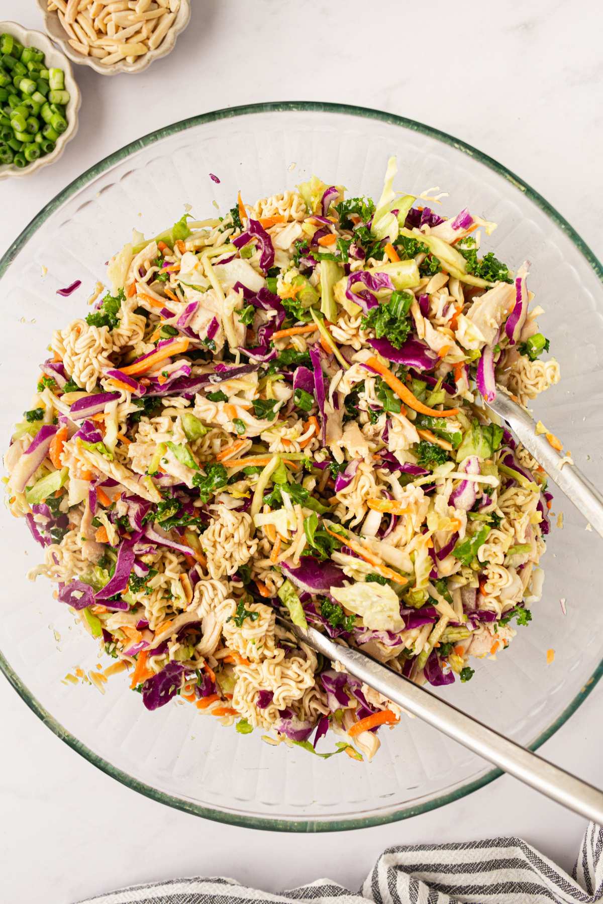 Using salad tongs to toss dressing with cabbage salad.