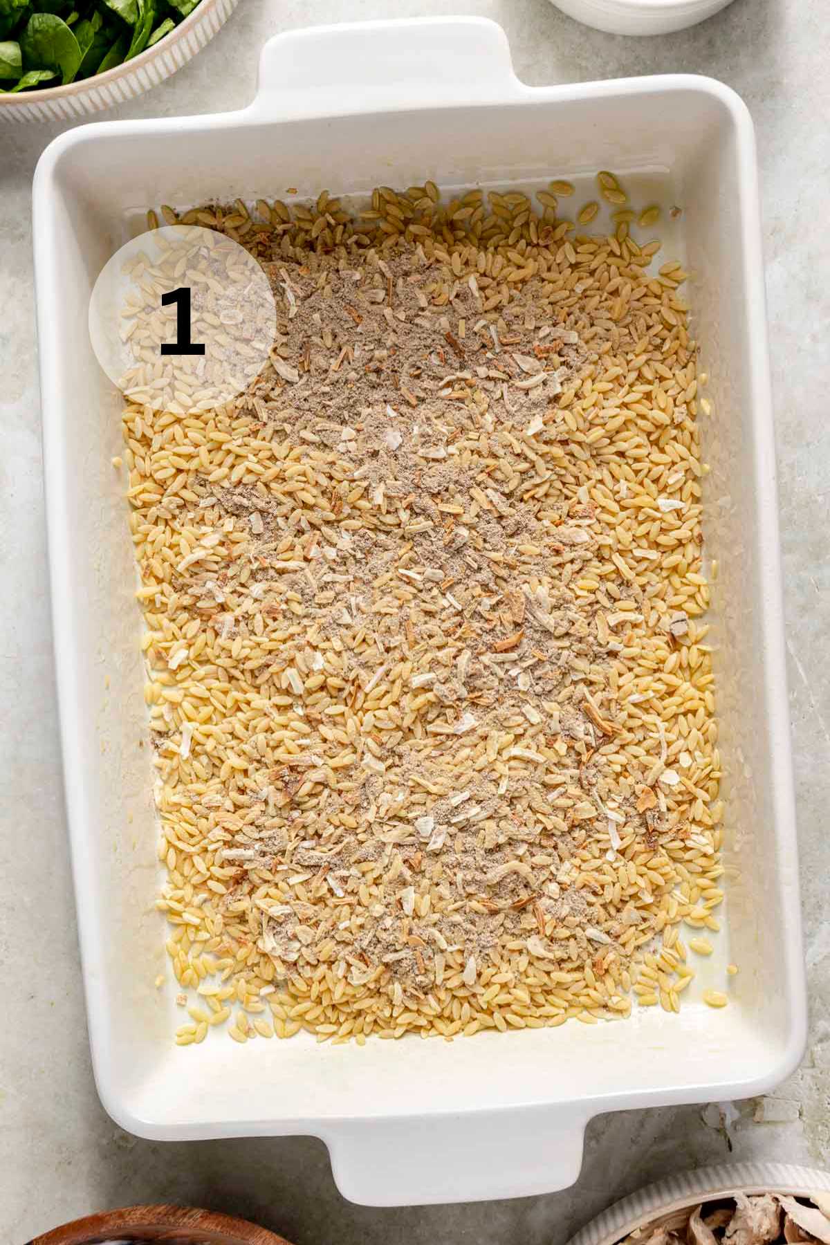 Uncooked orzo pasta with seasoning on top in a casserole dish.