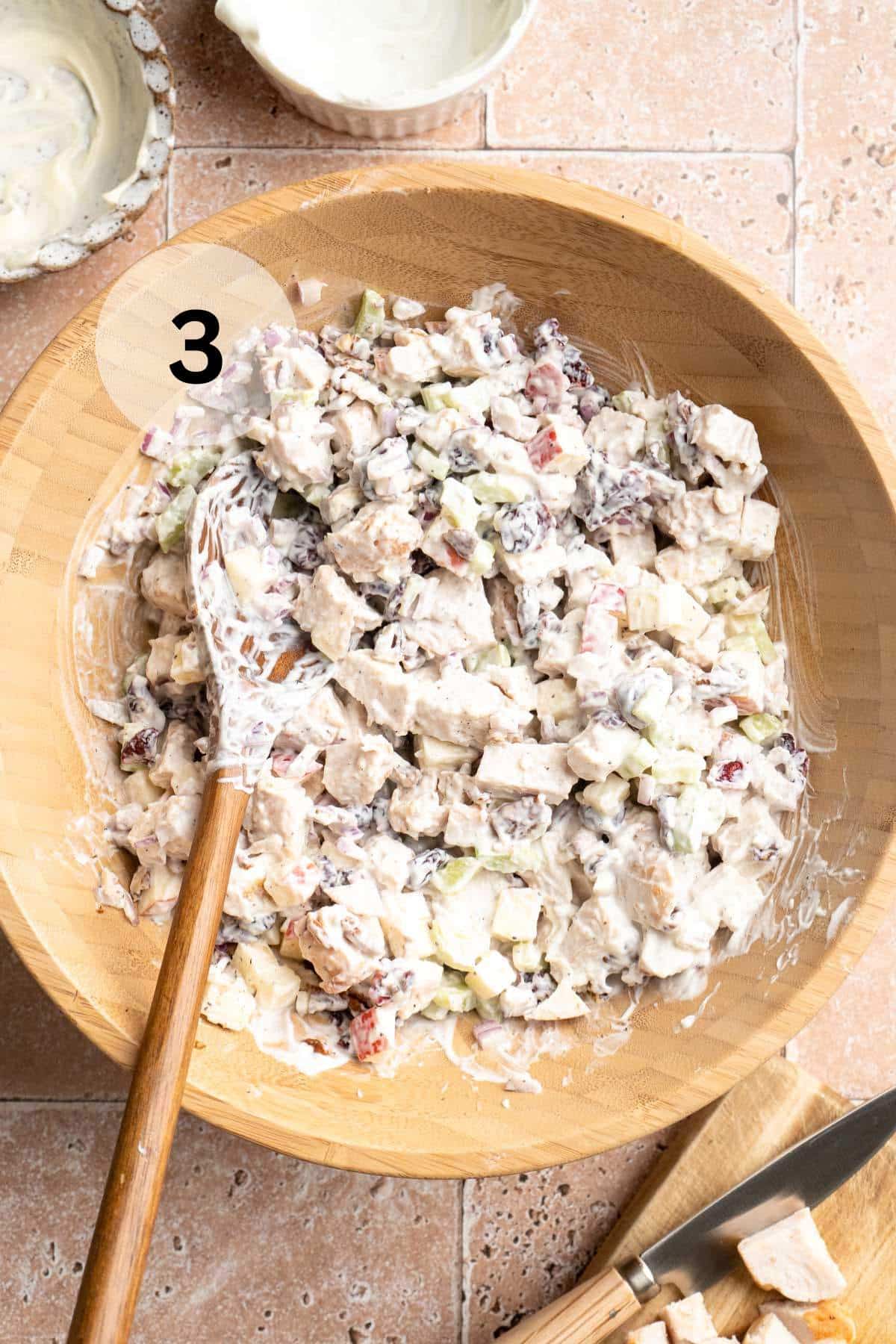 Stirring together chicken salad with dressing in a wooden bowl with a wooden spoon.