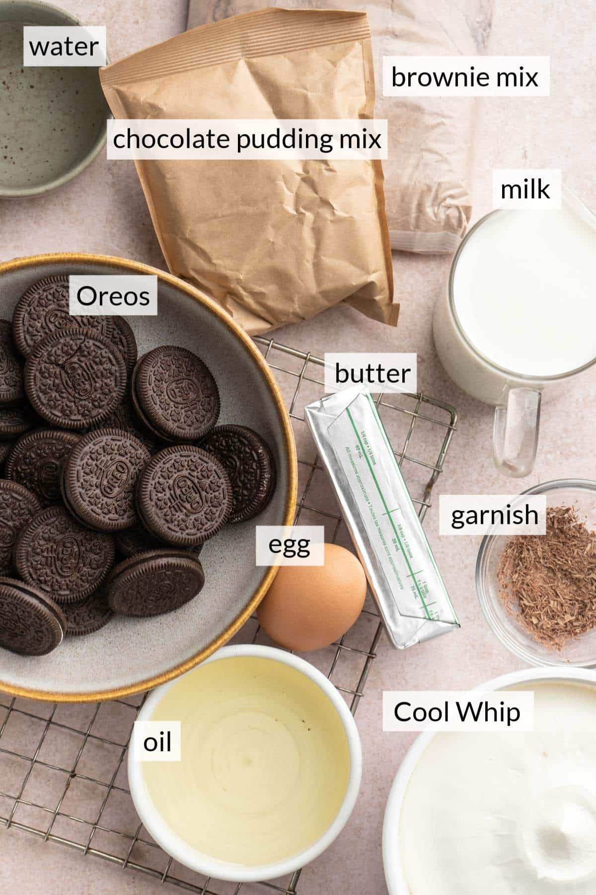 Package of brownie mix and pudding mix near bowls with Oreos, Cool Whip, milk and oil.