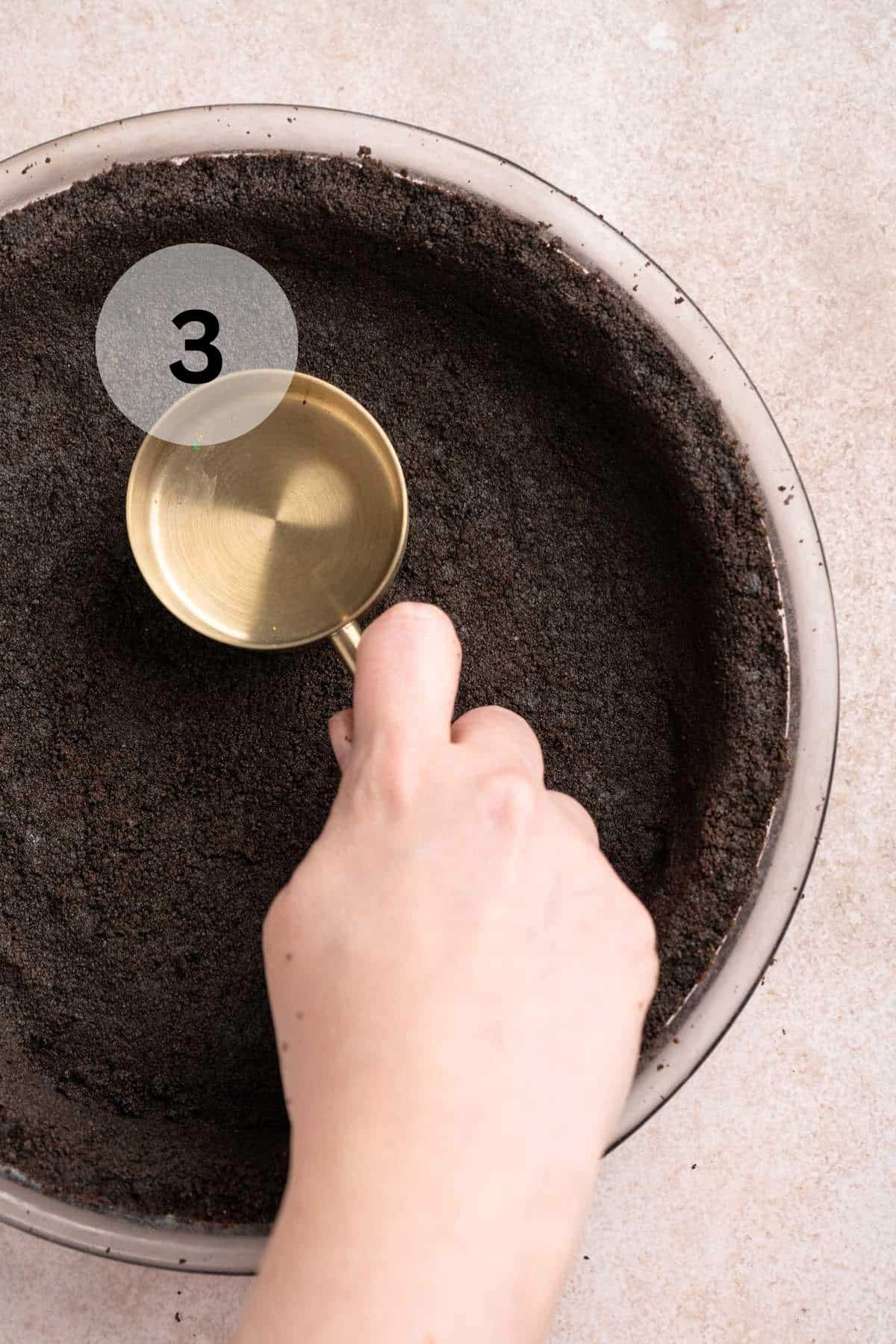 Pressing Oreo crumbs into a pie plate.