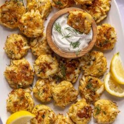 Baked Crab Cakes on a large white serving tray with dill sauce.