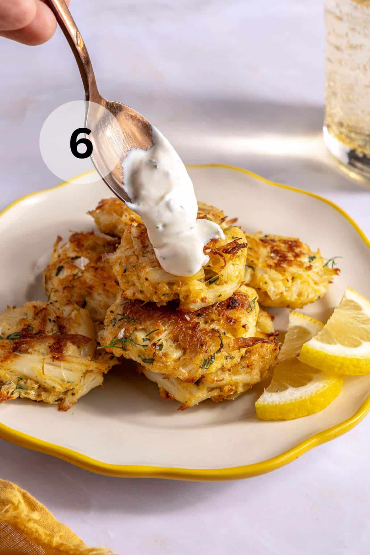 Spooning lemon dill sauce over baked crab cakes on a plate.