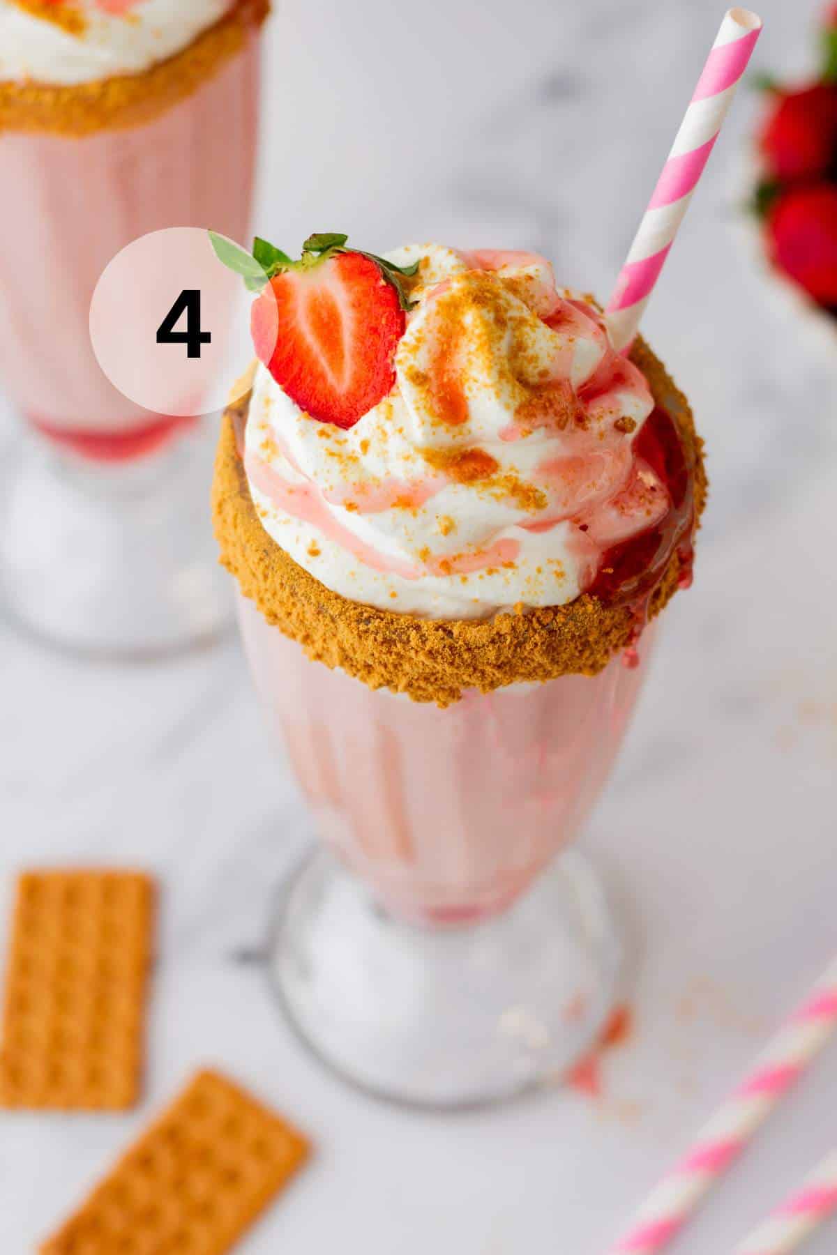 Strawberry milkshake topped with a strawberry and graham cracker crumbs.