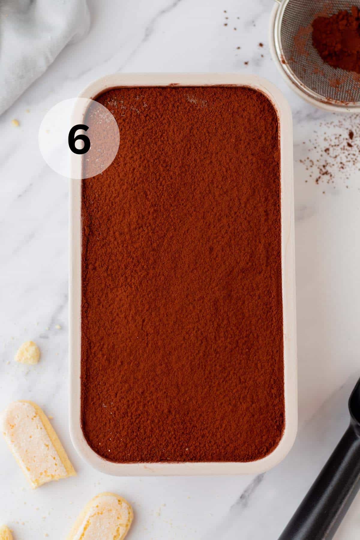 Ice cream mixture topped with cocoa powder in a loaf pan.