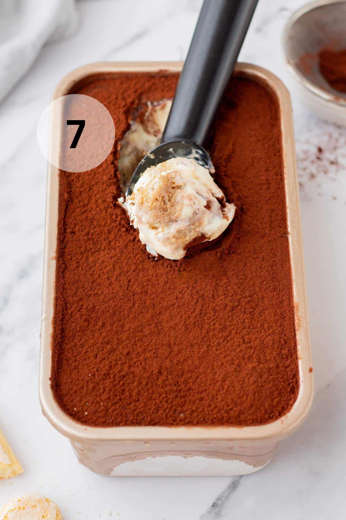 Scooping tiramisu ice cream from a loaf pan.