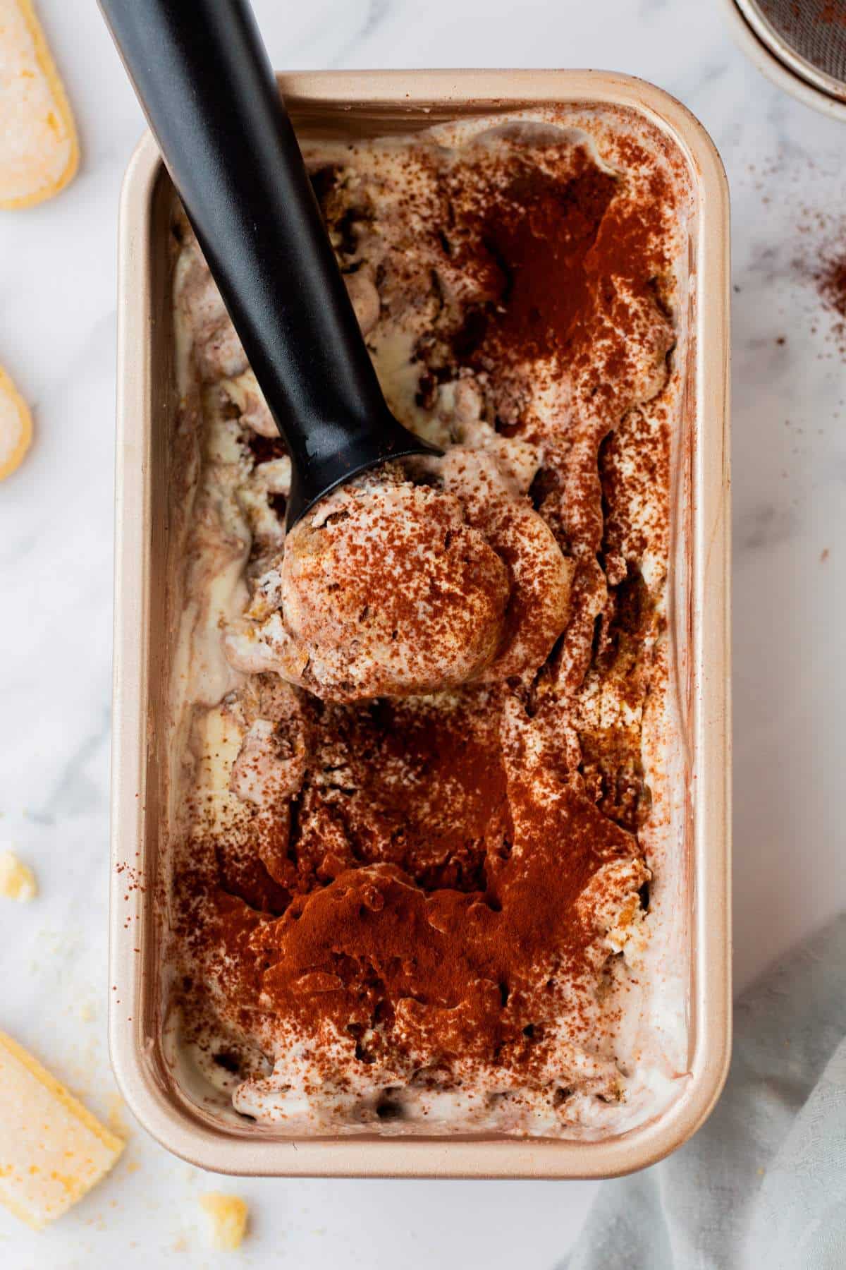 Scooping tiramisu ice cream from a loaf pan.