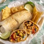 Burrito cut in half near another burrito in a basket lined with parchment.