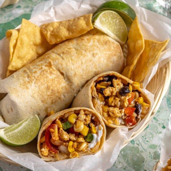 Burrito cut in half near another burrito in a basket lined with parchment.