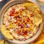 Tortilla chips in a corn dip topped with corn kernels and pico de Gallo.