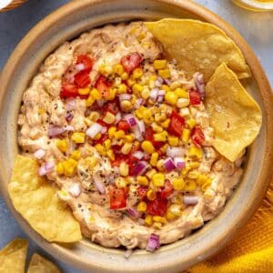 Tortilla chips in a corn dip topped with corn kernels and pico de Gallo.