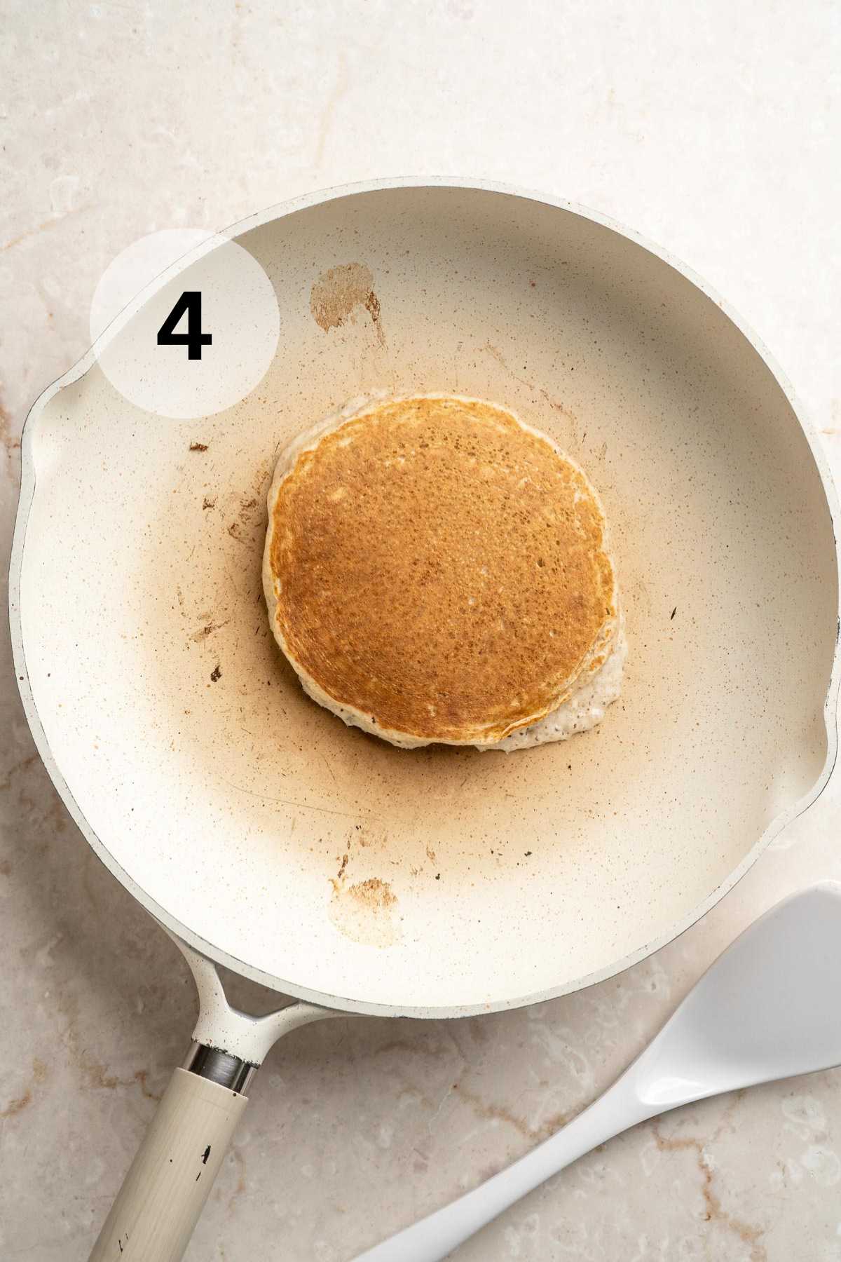 Flipped pancake cooking in a white pan.
