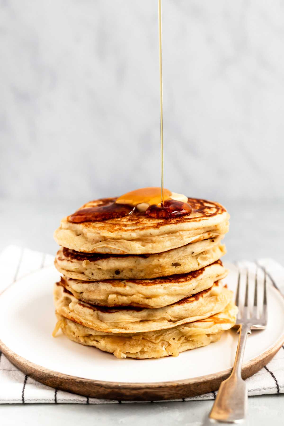 Drizzling syrup over a stack of buttermilk pancakes.