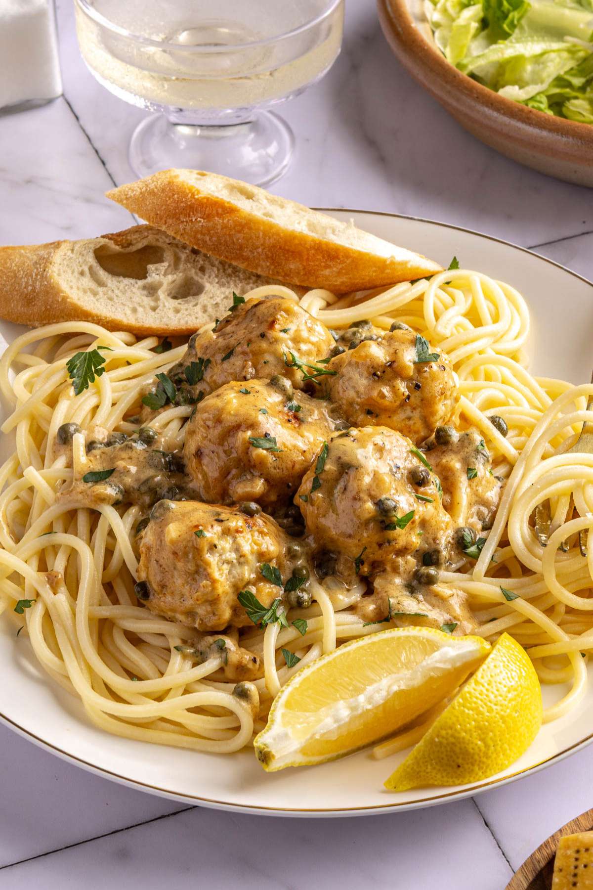 Chicken piccata meatballs served over pasta with lemon wedges.