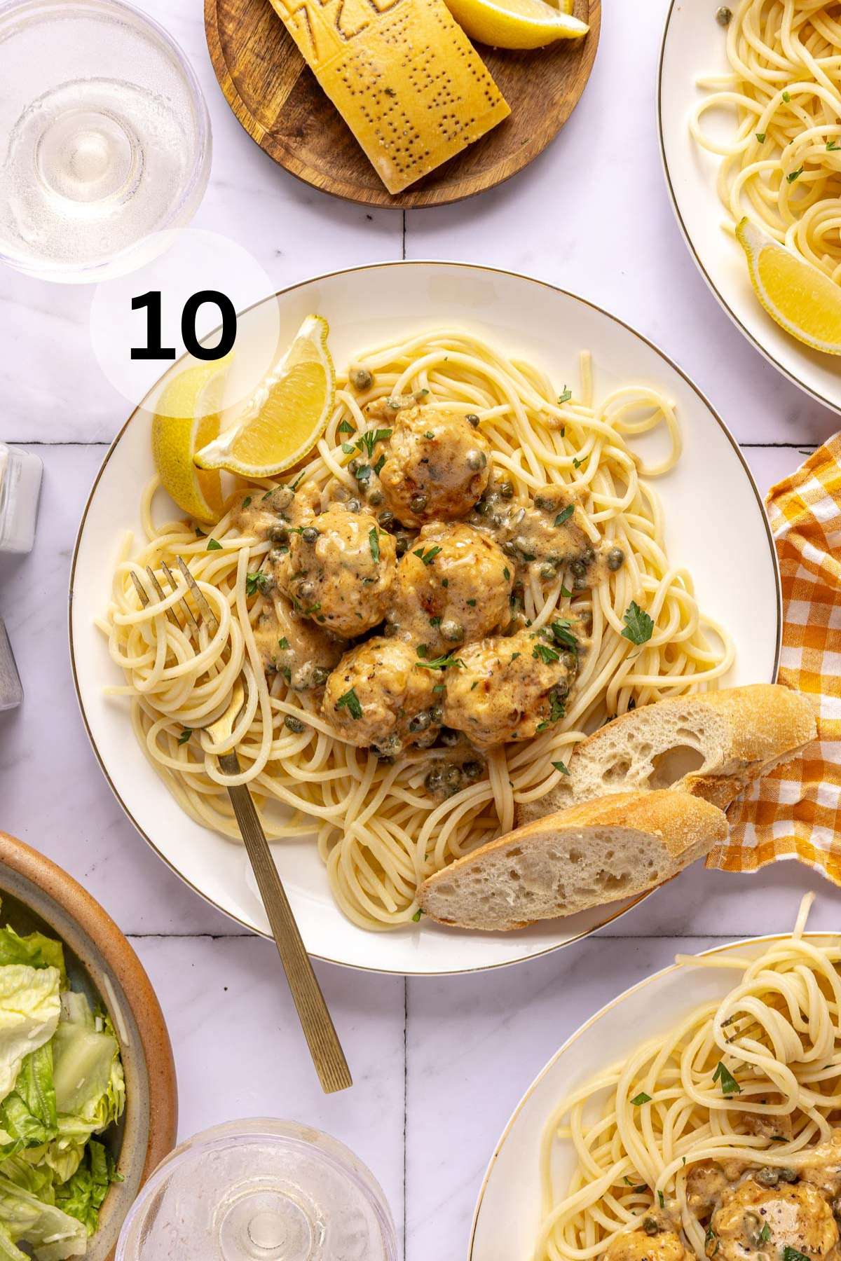 Chicken piccata meatballs with sauce served over pasta with slices of bread.