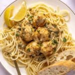 Chicken piccata meatballs served over spaghetti with bread.