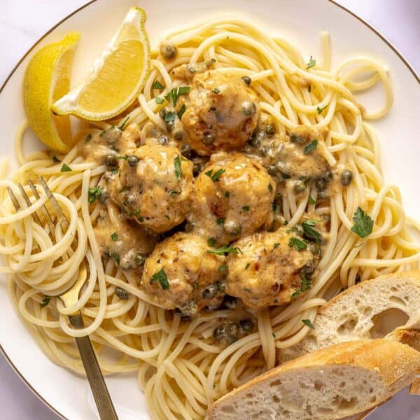 Chicken piccata meatballs served over spaghetti with bread.