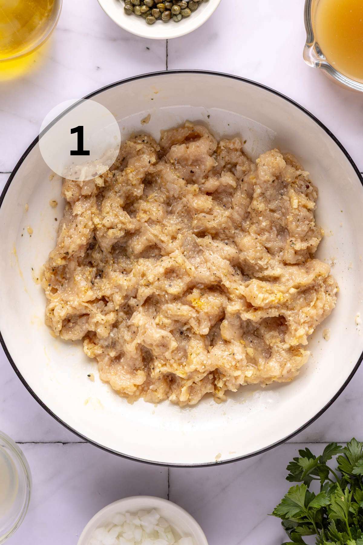 Ground chicken mixed with egg, breadcrumbs and seasonings in a white bowl.