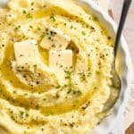 White serving bowl filled with creamy mashed potatoes and a serving spoon.