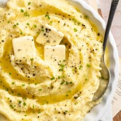 White serving bowl filled with creamy mashed potatoes and a serving spoon.