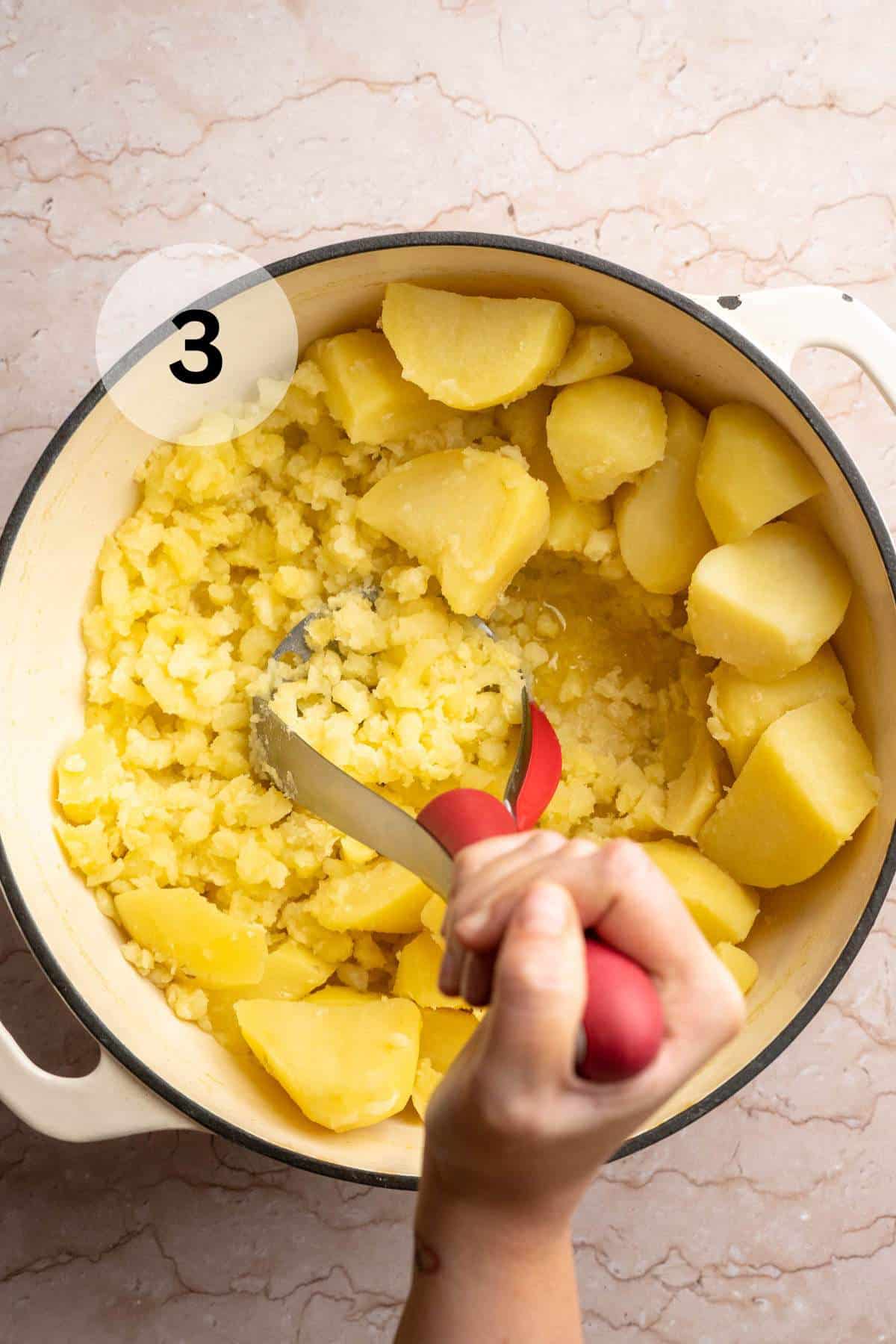 Using a potato masher to mash potatoes in a pot.