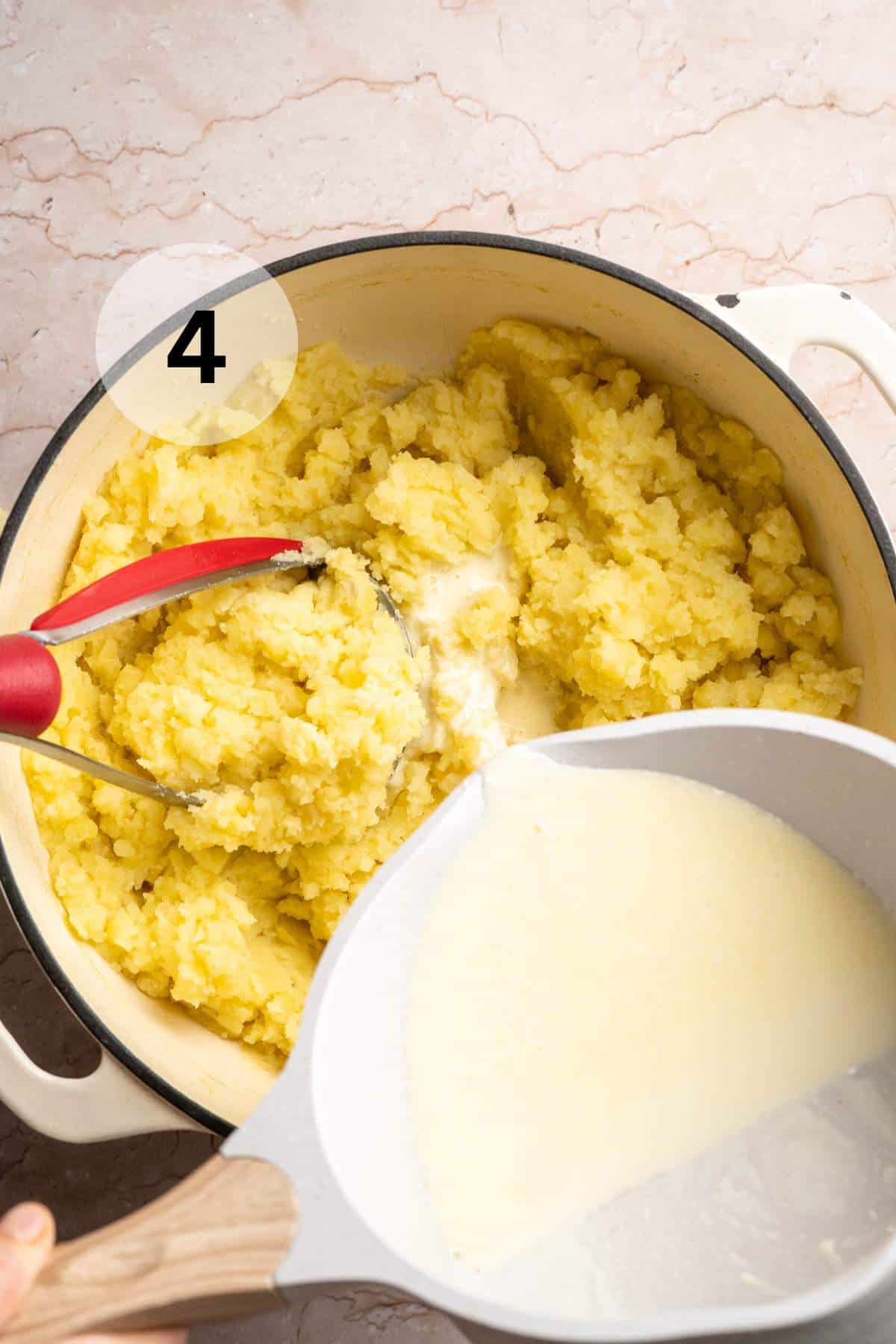 Pouring cream into partially mashed potatoes.