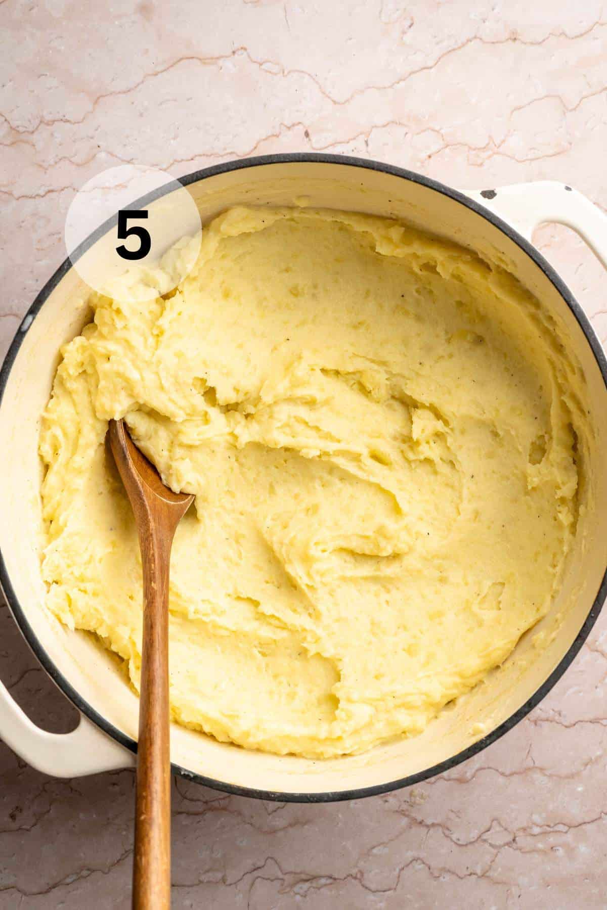 Using a wooden spoon to stir mashed potatoes in a large pot.