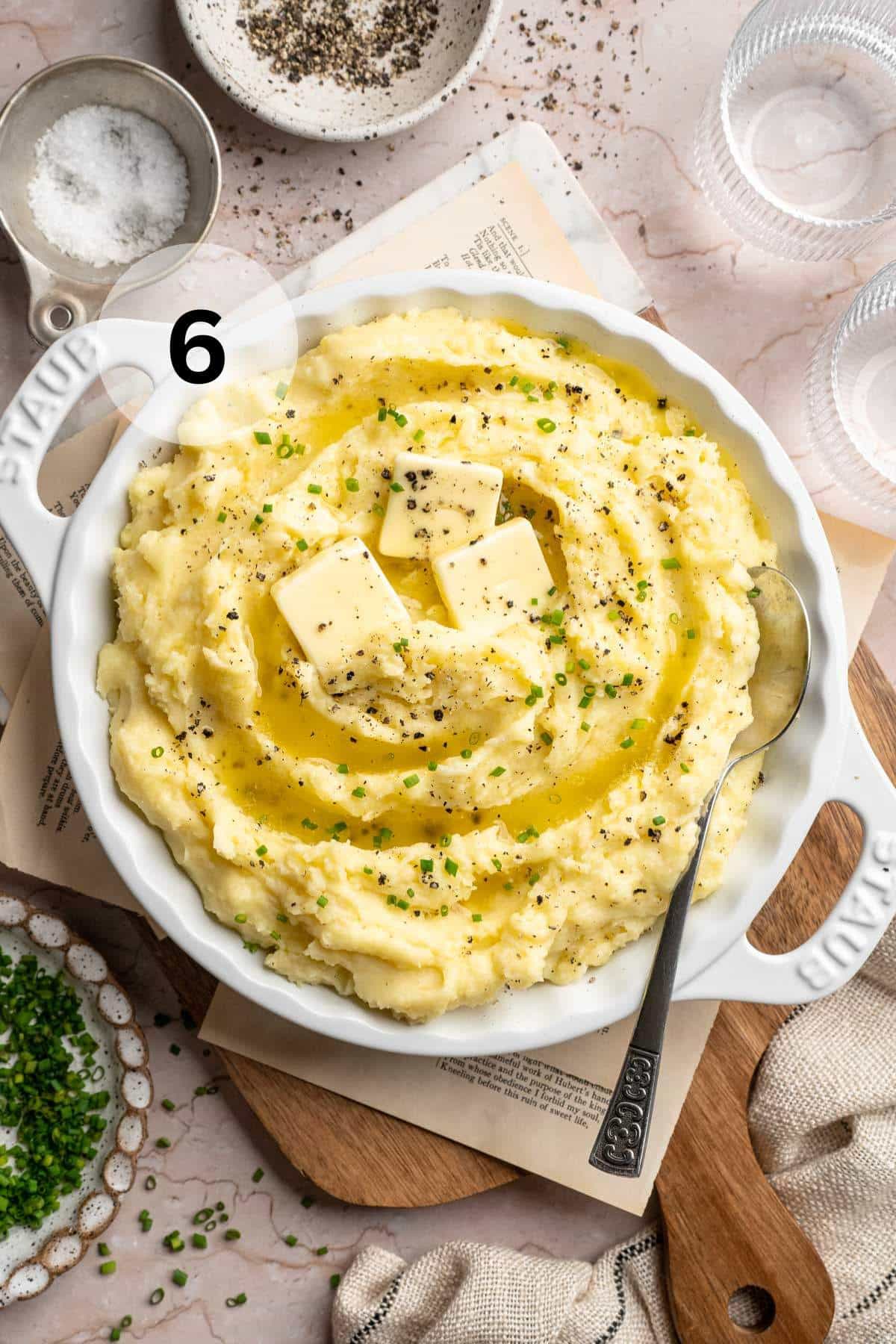 A white serving bowl filled with mashed potatoes and topped with butter.