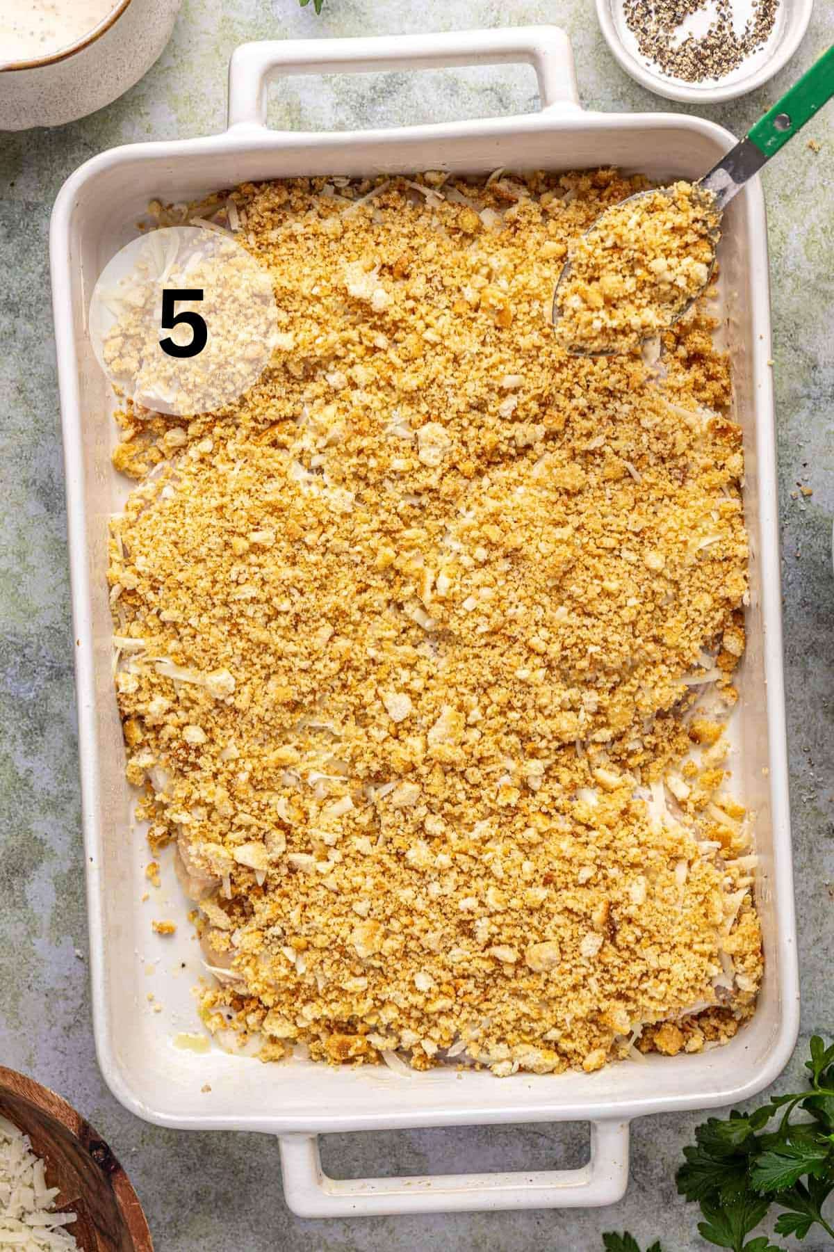 Chicken breasts breaded with crushed crouton mixture in a white dish.