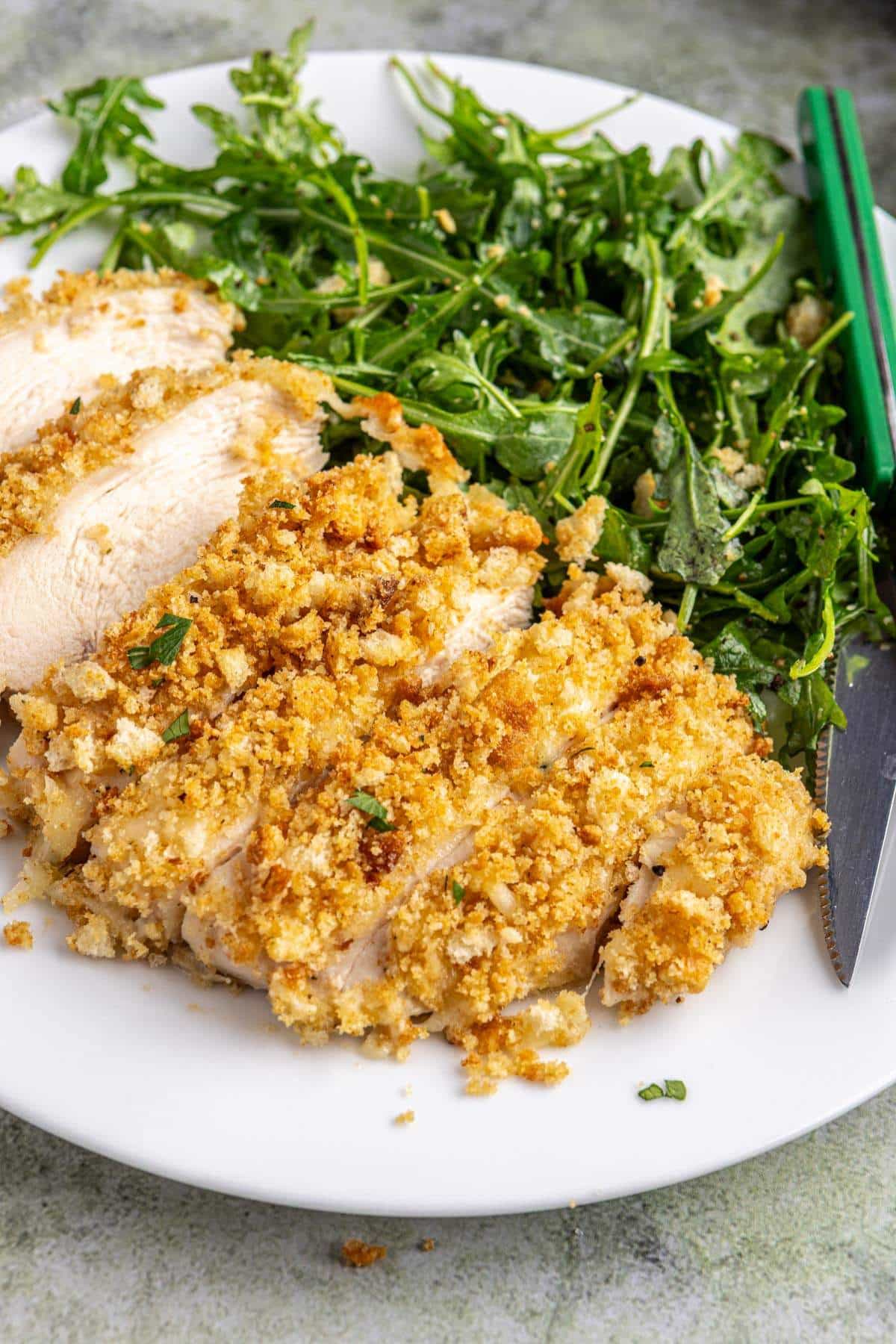 Caesar dressing chicken served with a green salad on a white plate.