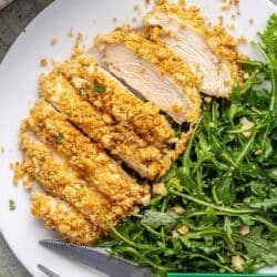 Breaded caesar dressing chicken on a white plate with a simple arugula salad.