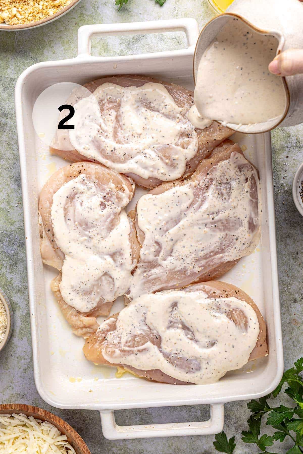 Chicken breasts covered with caesar dressing in a white casserole dish.