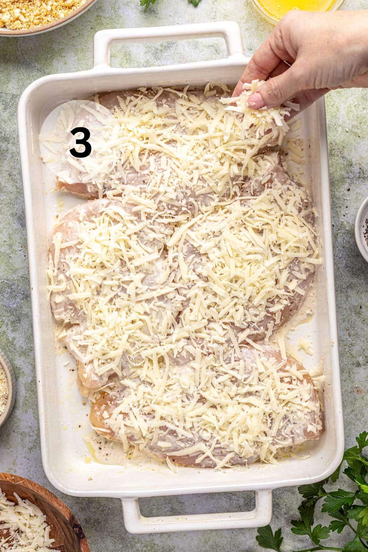 Sprinkling shredded mozzarella over chicken breasts in a baking dish.