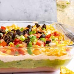 7-layer dip in a glass dish with layers of bean dip, guacamole, sour cream and cheese.