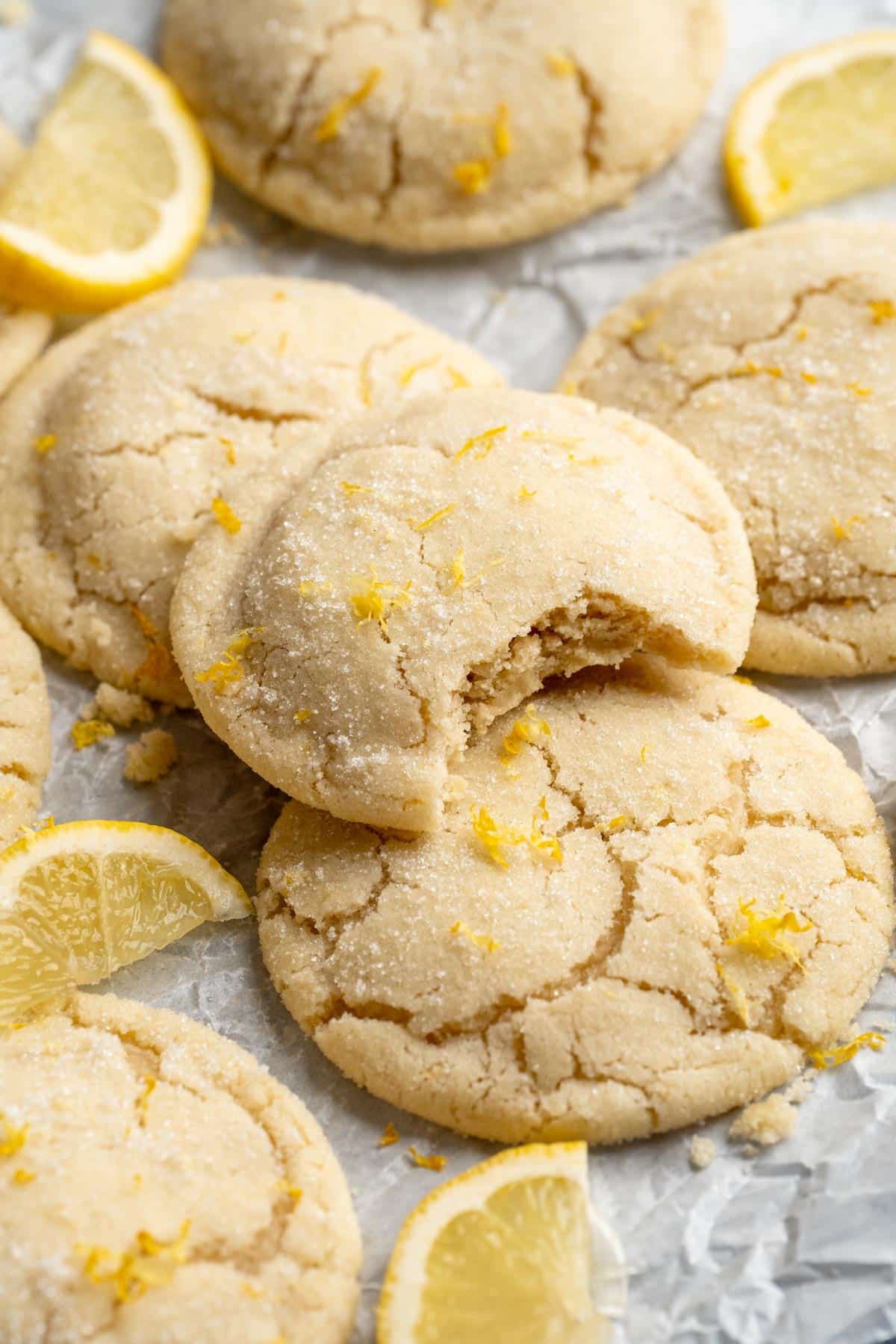 Lemon cookies on parchment and one has a bite taken out.