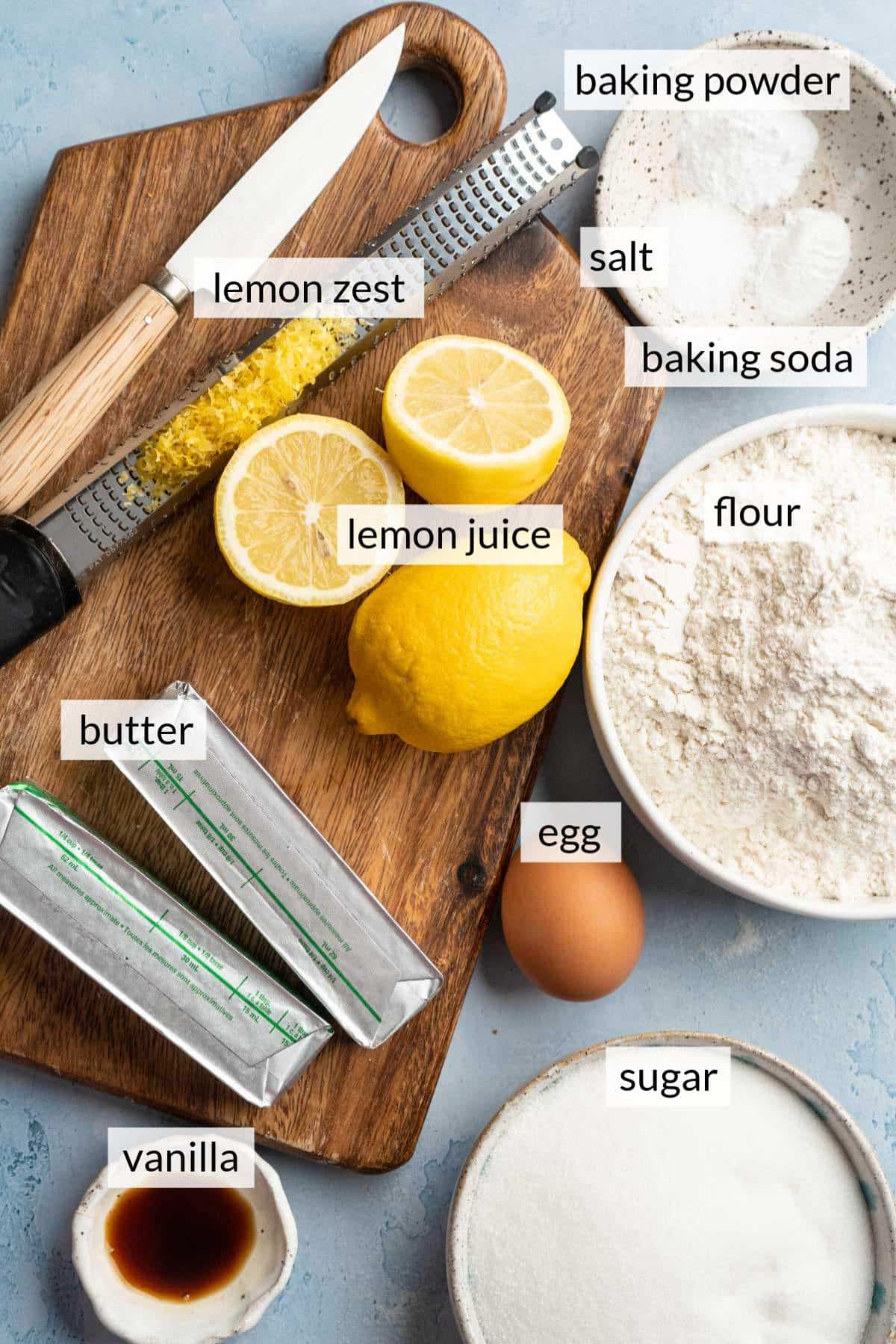 Lemons near bowls of sugar, flour, vanilla and salt.