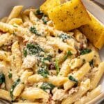 Tuscan chicken pasta served in a bowl with garlic bread.