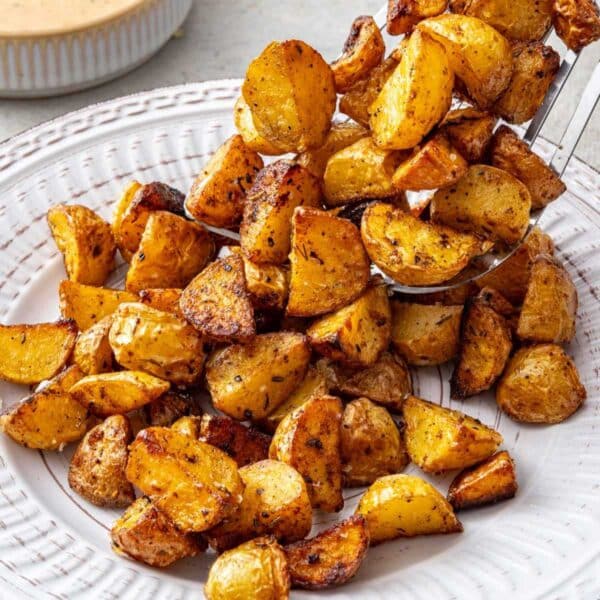 Scooping pan fried potatoes onto a white plate.