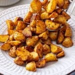 Scooping pan fried potatoes onto a white plate.