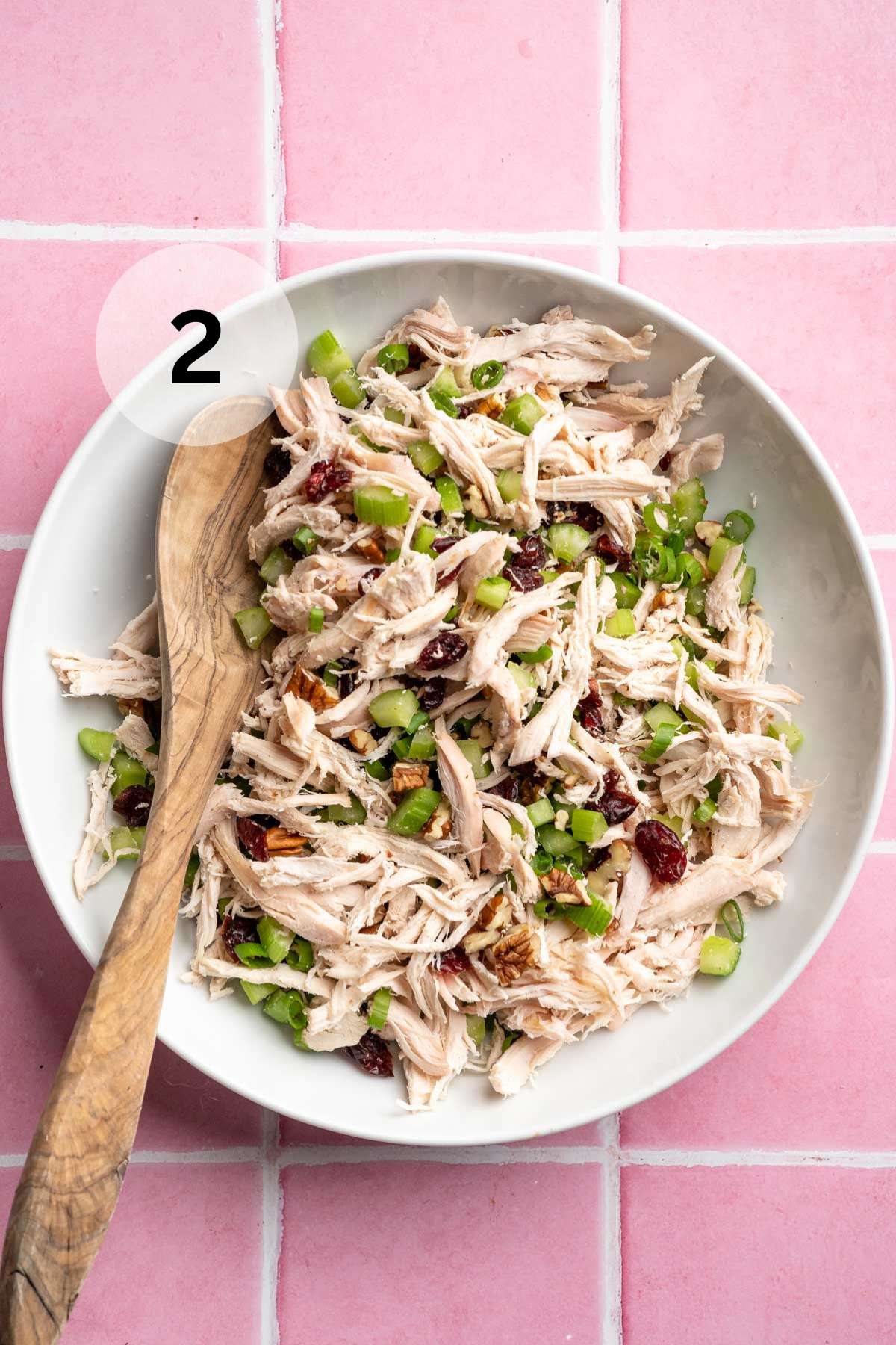 Using a wooden spoon to stir shredded chicken with chopped celery, green onion and cranberries.